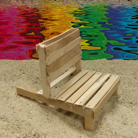 A wooden chair on a beach with a multicolor sea behind it.